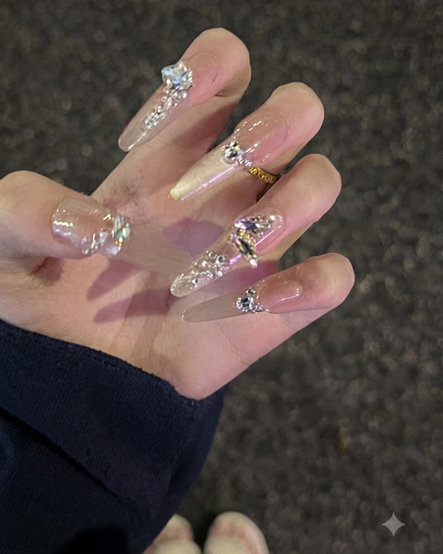 Una vista ravvicinata di una mano con unghie lunghe nude borchiate di strass incurvate leggermente per mostrare il profilo.