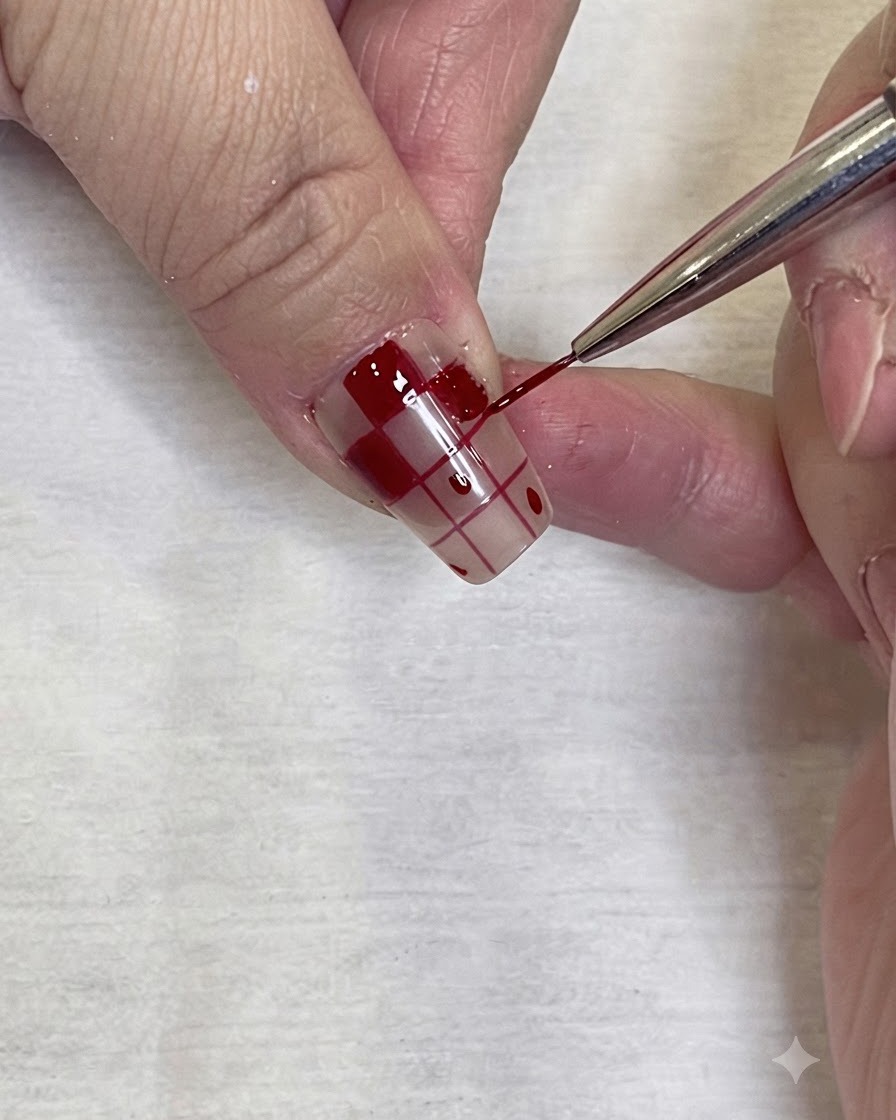 Un primo piano dettagliato di un pennello fine da nail art che applica con precisione lo smalto gel rosso sul bordo di un motivo a quadri su ununghia.