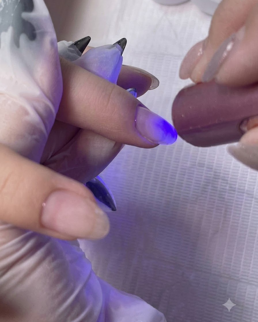 Una mini lampada UV/LED portatile che polimerizza lo strato di gel base sul dito di una cliente.