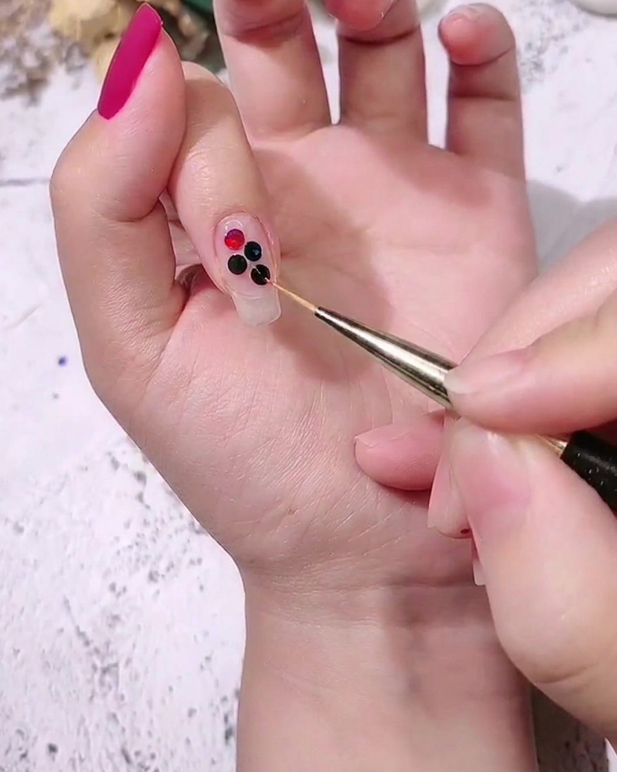 Primo piano di una mano che posiziona paillettes a pois colorate di medie dimensioni accanto a quelle più grandi su ununghia usando un pennello di precisione.
