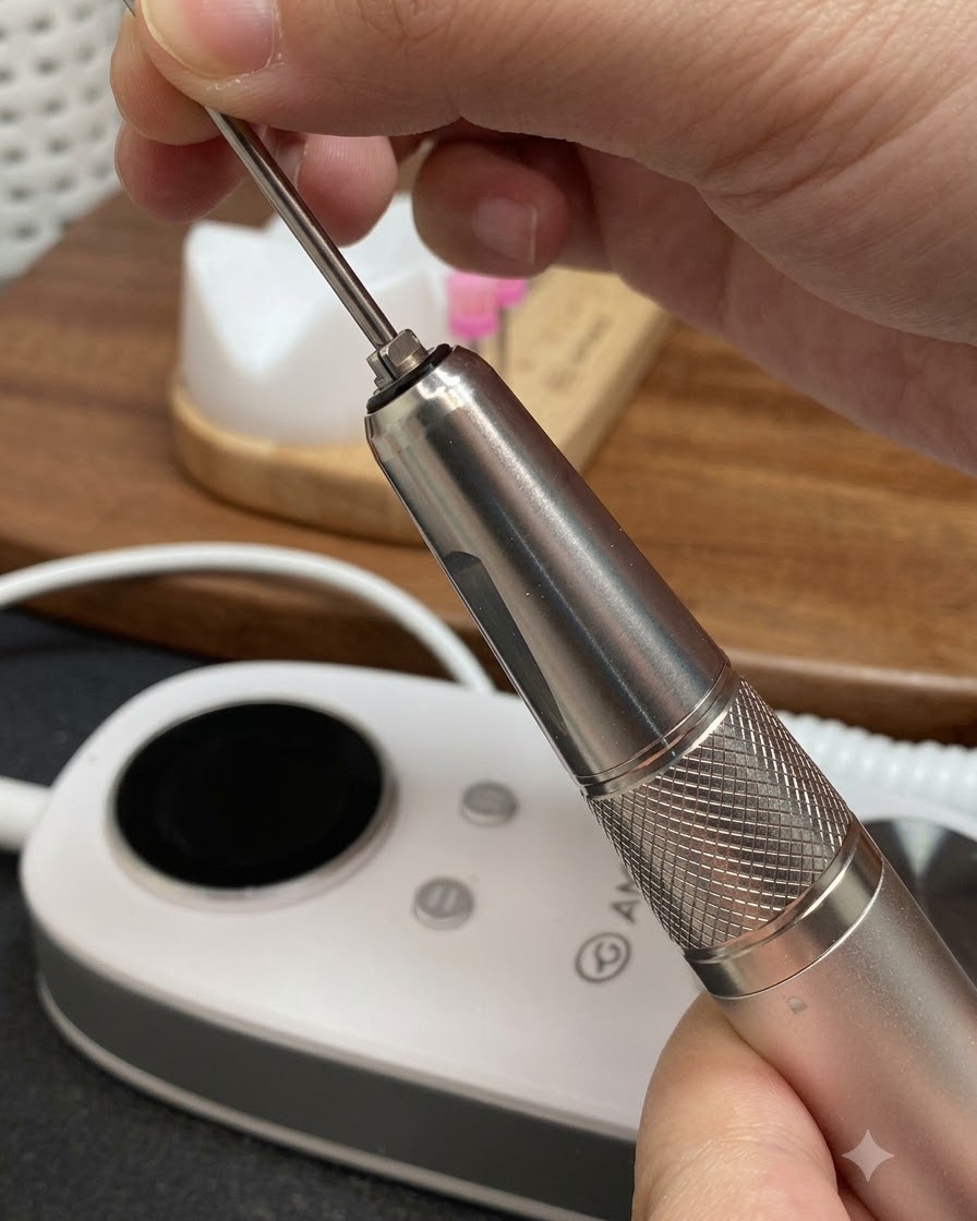Mani che inseriscono una punta per fresa in metallo lunga e conica nel manipolo di una lima per manicure elettrica.