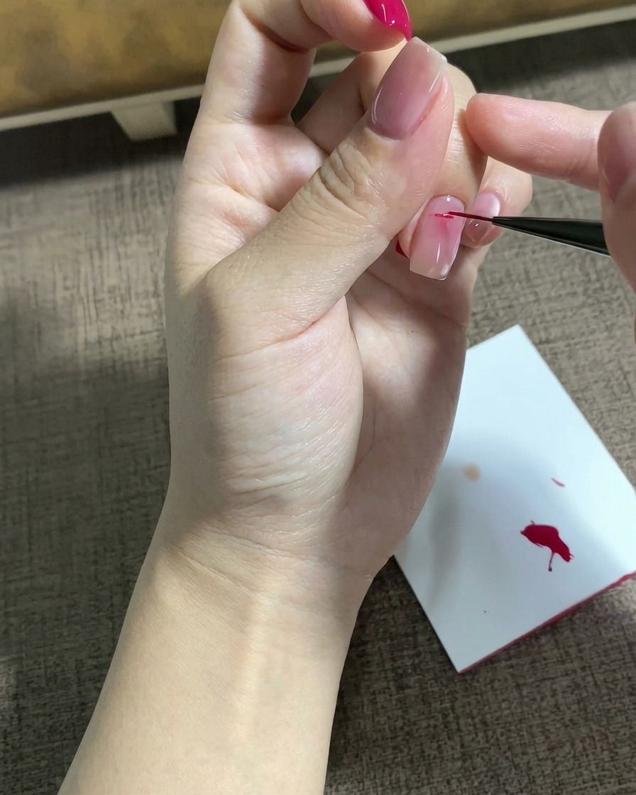 Un pennello liner sottile disegna un motivo a stella magenta dettagliato sulla superficie di ununghia preparata.