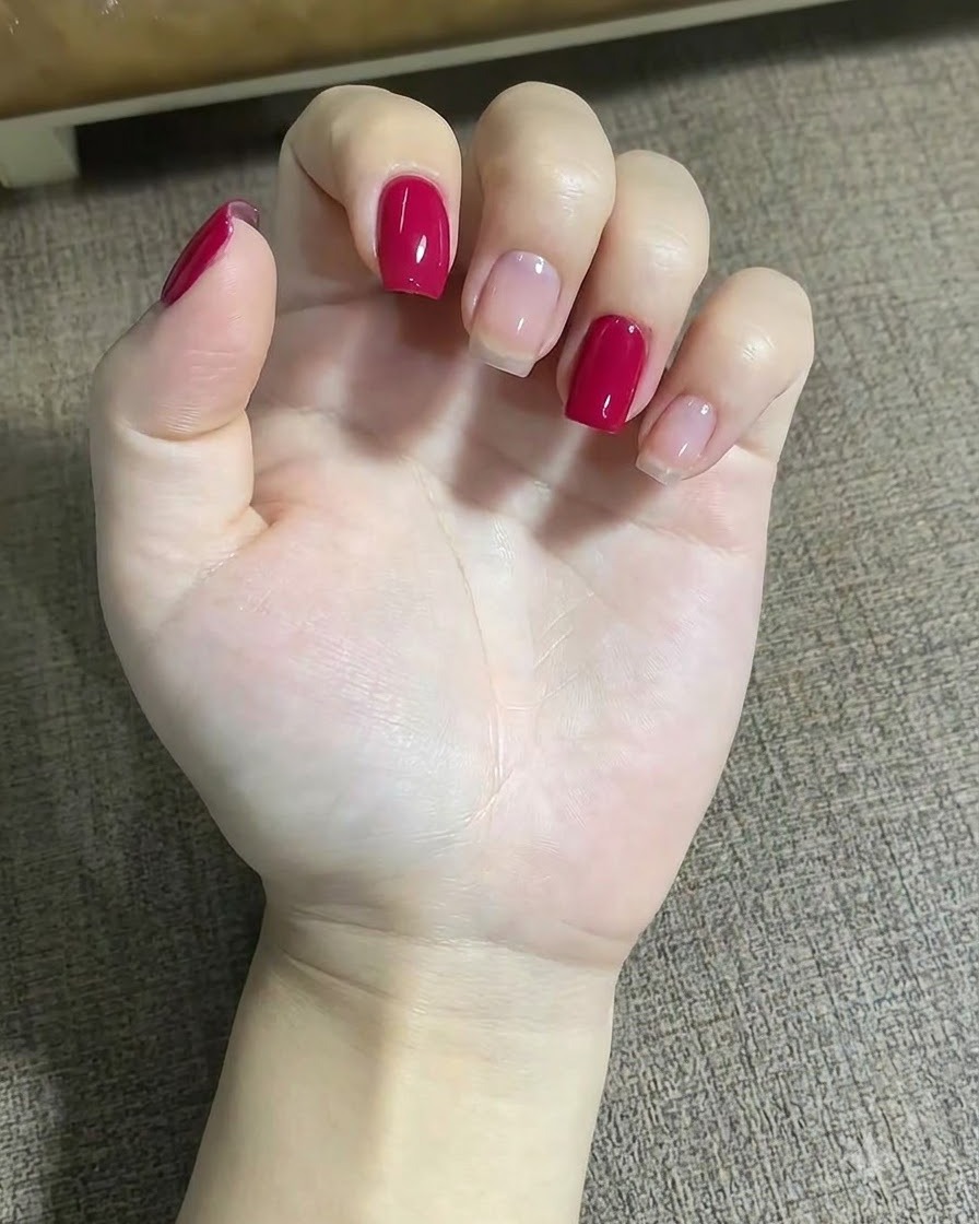 Un primo piano di una mano che usa un pennello liner sottile per applicare piccoli punti rossi vicino al design a stella sul dito medio.