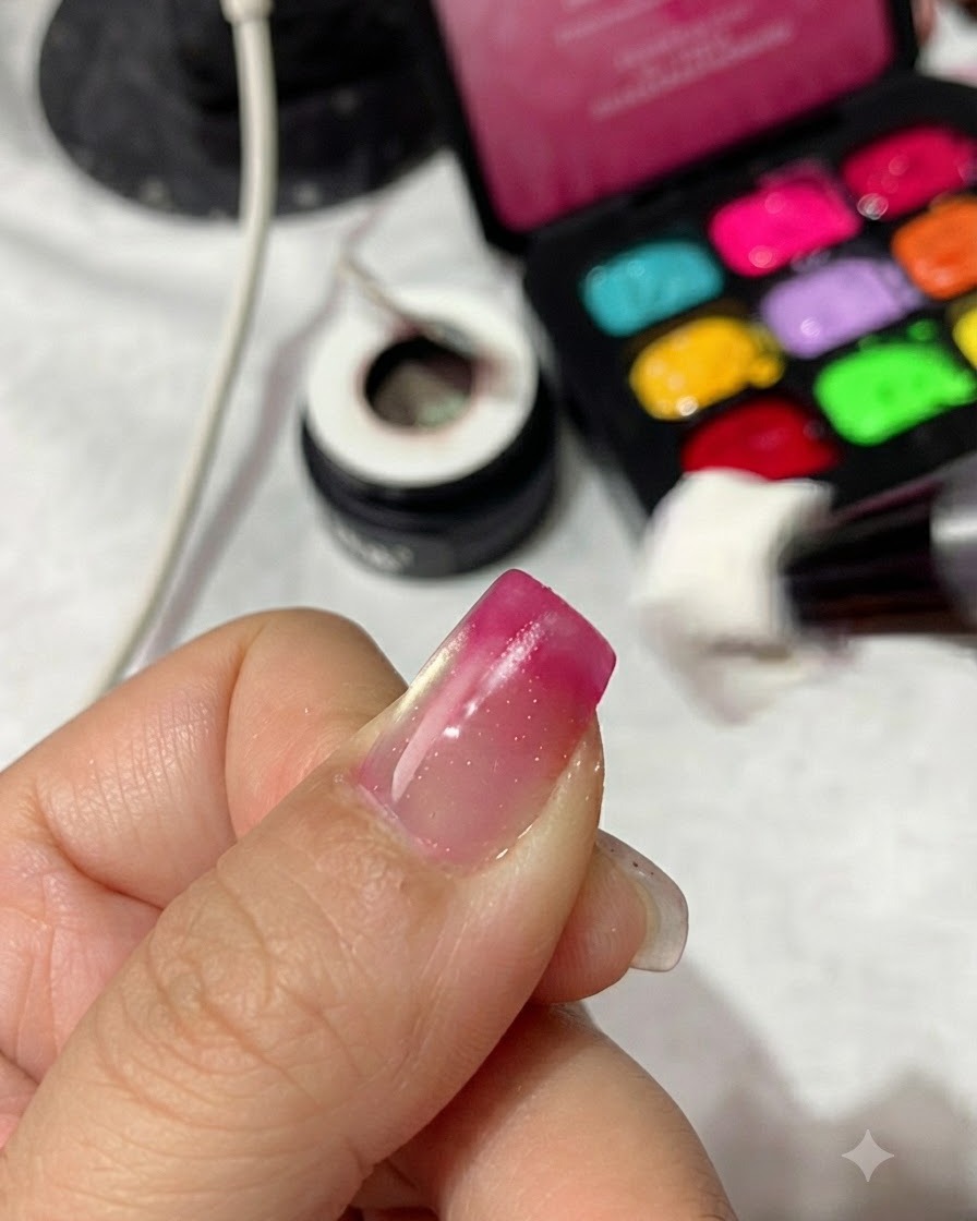 Un applicatore a spugnetta che tampona smalto gel rosso magenta sulla punta di ununghia per creare una sfumatura.