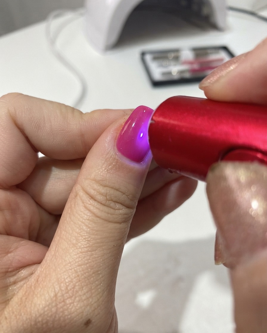 Una lampada UV/LED portatile rossa che polimerizza lo smalto gel su ununghia.