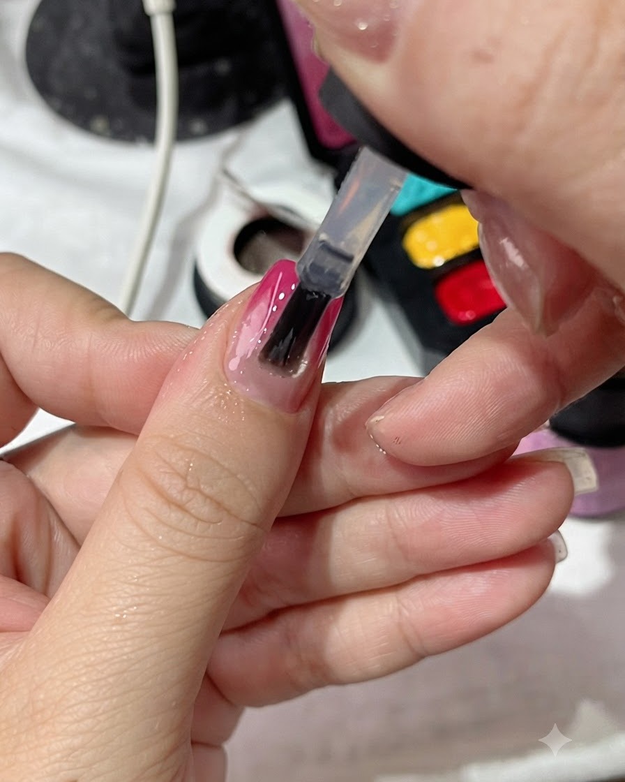 Un pennello da smalto che applica uniformemente un top coat trasparente su ununghia con manicure sfumata.