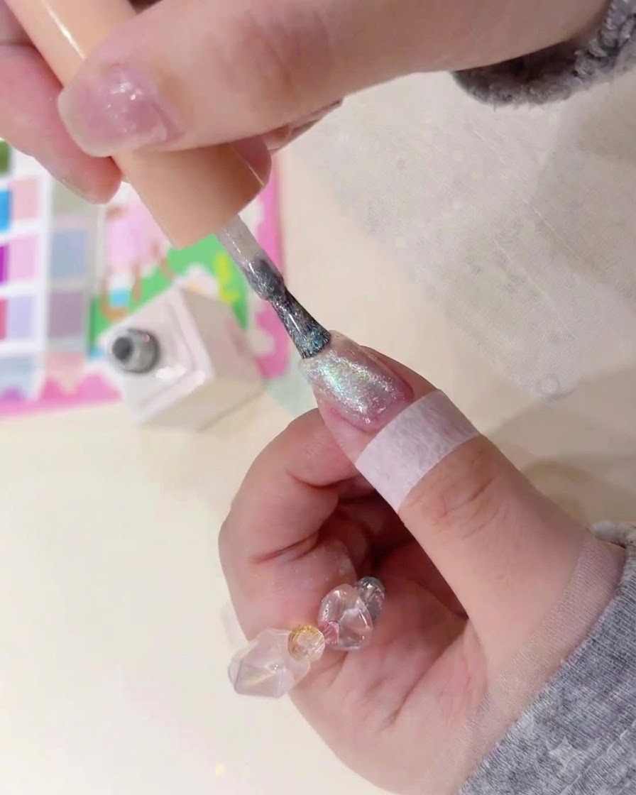 Un pennello applica del gel magnetico ambrato e brillante su ununghia naturale.
