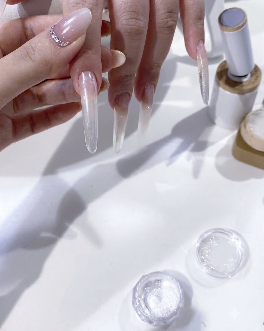 Una vista in primo piano di un pennello che applica con attenzione il pigmento in gel bianco per modellare una french tip su ununghia estesa.