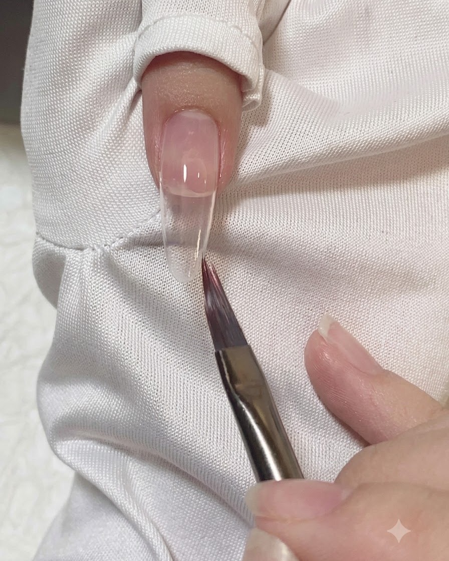 Un pennello piatto che leviga e sfuoca i bordi del gel rosa su ununghia.