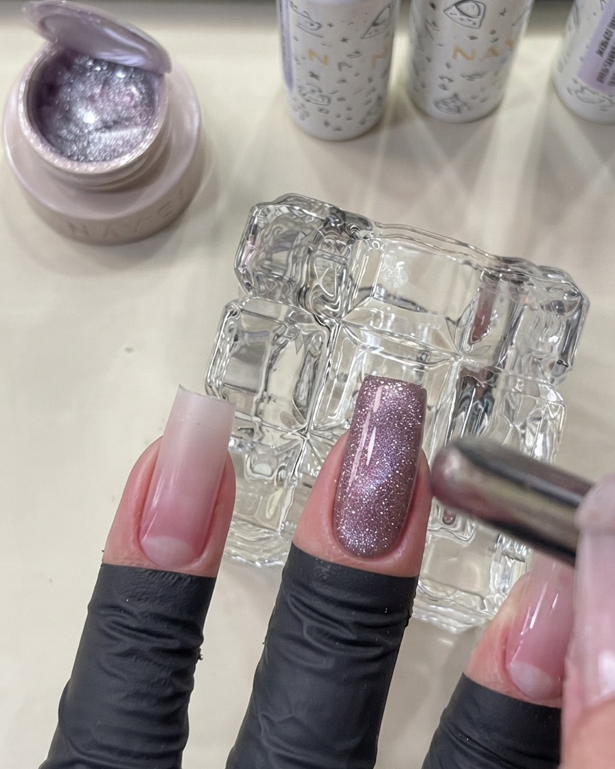 Uno strumento magnetico tenuto vicino a ununghia per modellare il gel cat eye in un effetto perlato luminoso.