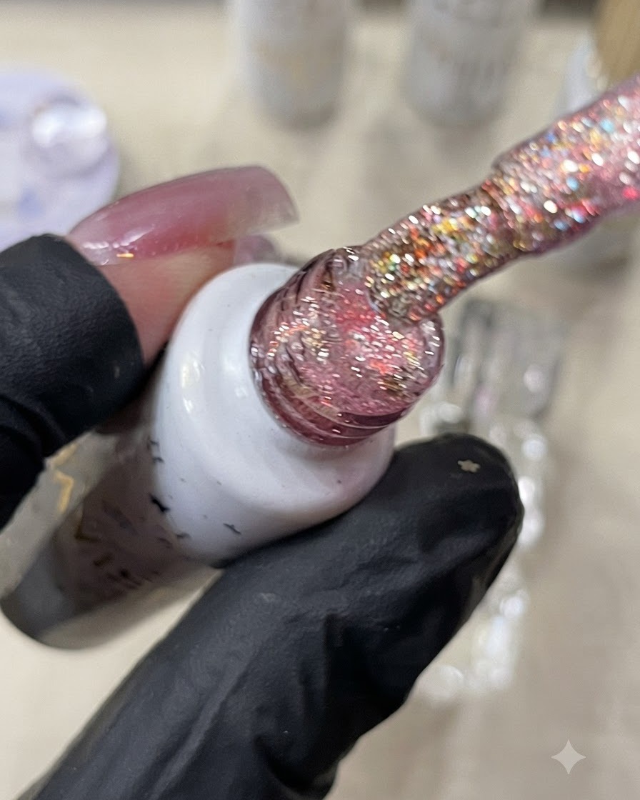 Un pennello che tiene del gel glitter arancione caldo sopra ununghia.