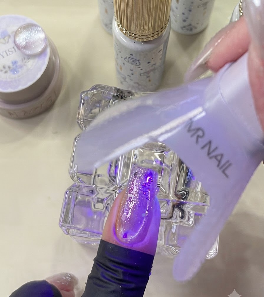 Una mini lampada UV che polimerizza ununghia decorata sotto una luce viola.