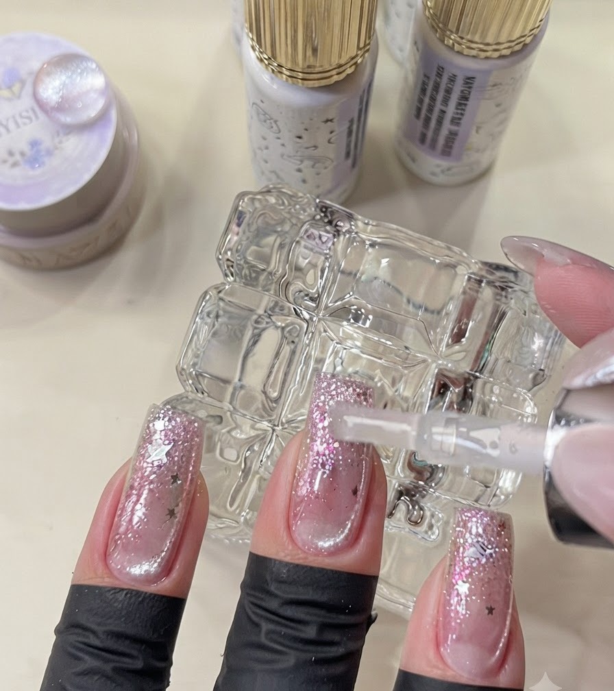 Un pennello che applica il top coat finale su unghie completate in stile galassia.