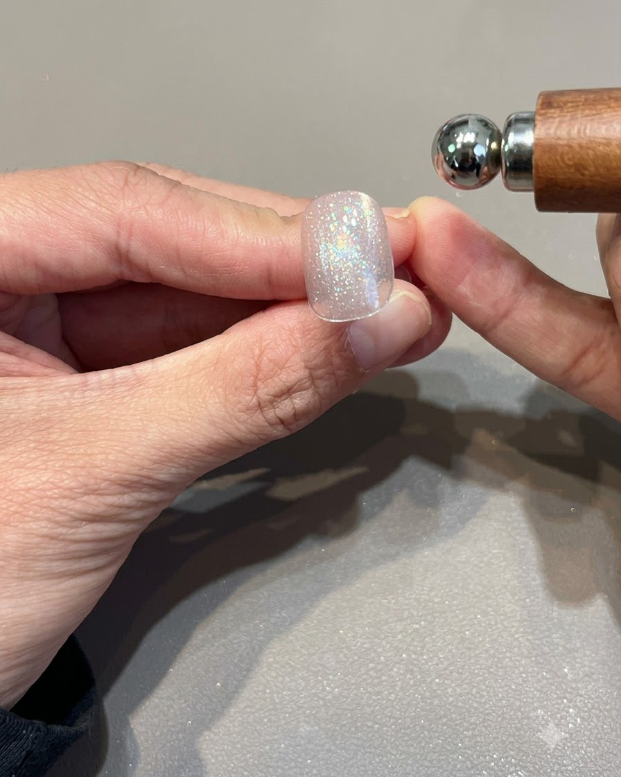 Un magnete sferico tenuto vicino a ununghia in gel cat eye rosa oro brillante per modellare la fascia di luce.