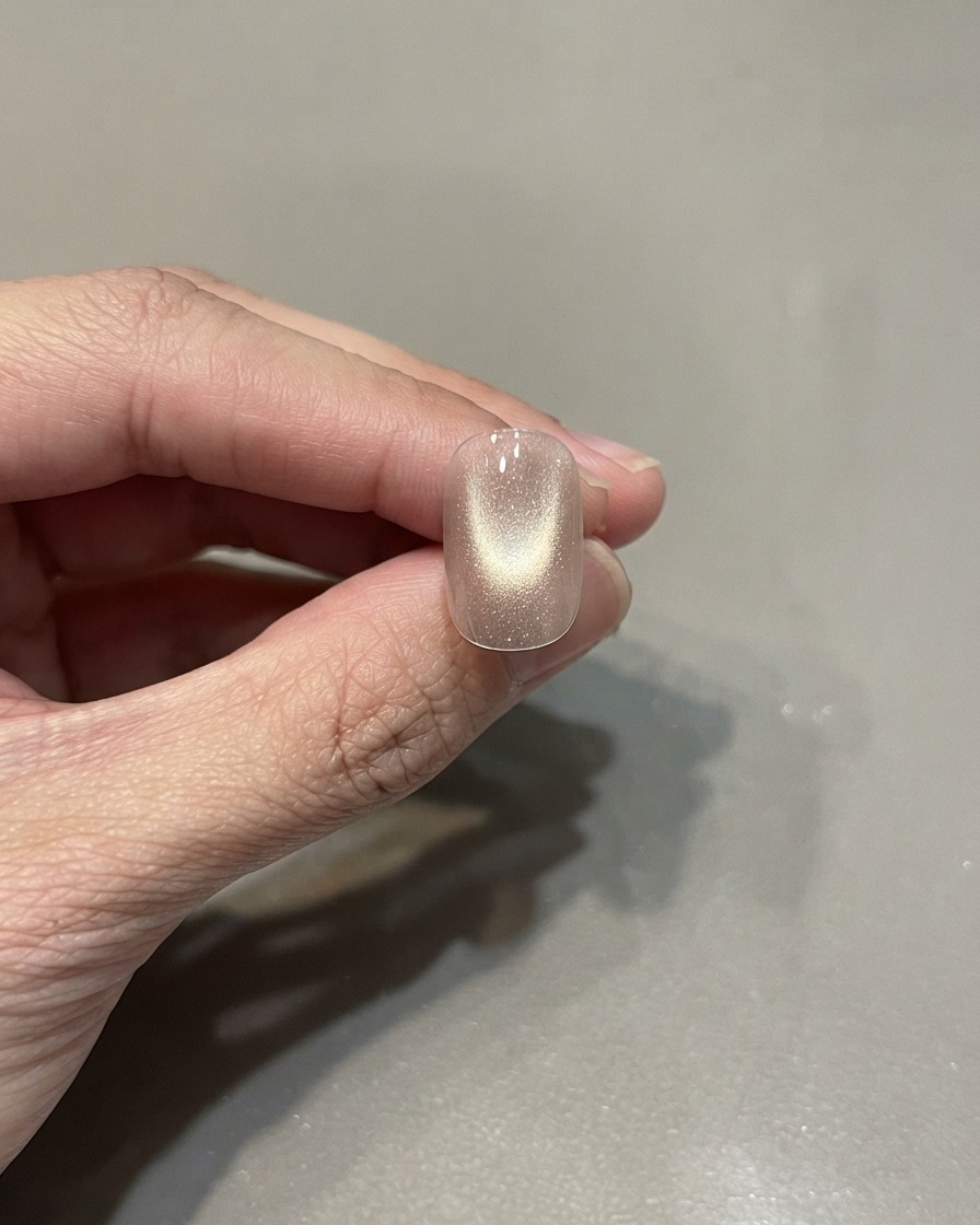Una singola unghia curata che mostra uno smalto cat eye rosa oro polimerizzato con un riflesso di luce centrato.