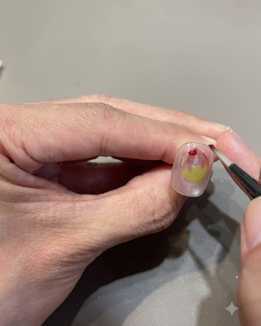 Uno scatto ravvicinato di un pennello fine che aggiunge una goccia di gel vetro rosso per migliorare la sfumatura della fragola.