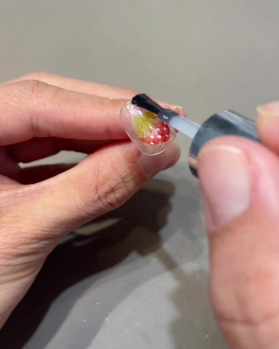 Un pennello che applica un top coat trasparente sopra ununghia decorata.