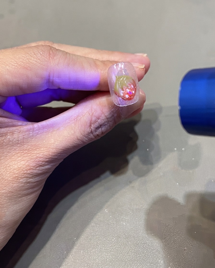 Una torcia UV portatile che polimerizza un design di unghia con fragola 3D.