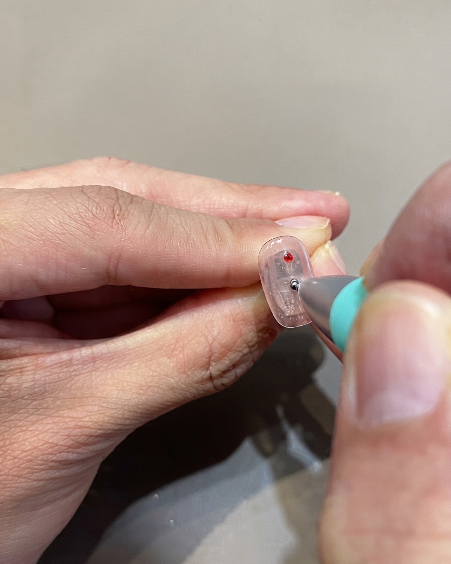 Un dotting tool che posiziona pois in gel vetro rosso su una superficie ungueale trasparente.