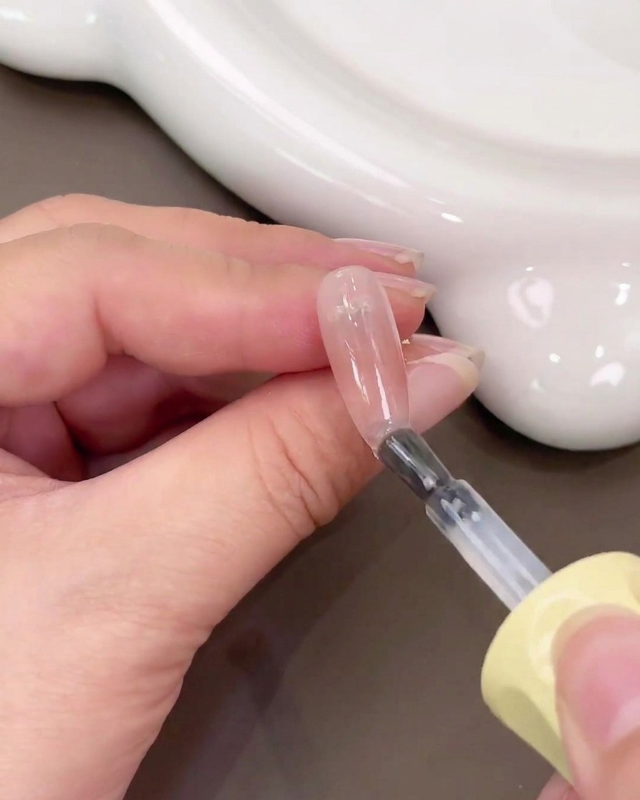 Un pennello che applica il gel base trasparente su ununghia con un gradiente blush rosa.