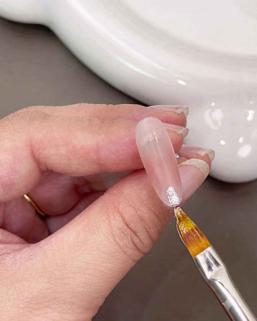 Un pennello sottile che applica gel bianco scintillante sulla punta di ununghia.