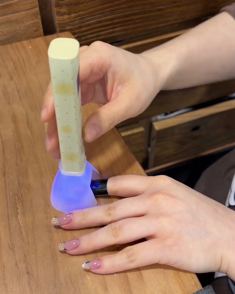 Una lampada per unghie UV/LED viola portatile che polimerizza il gel su ununghia mentre altre dita curate riposano sul tavolo.