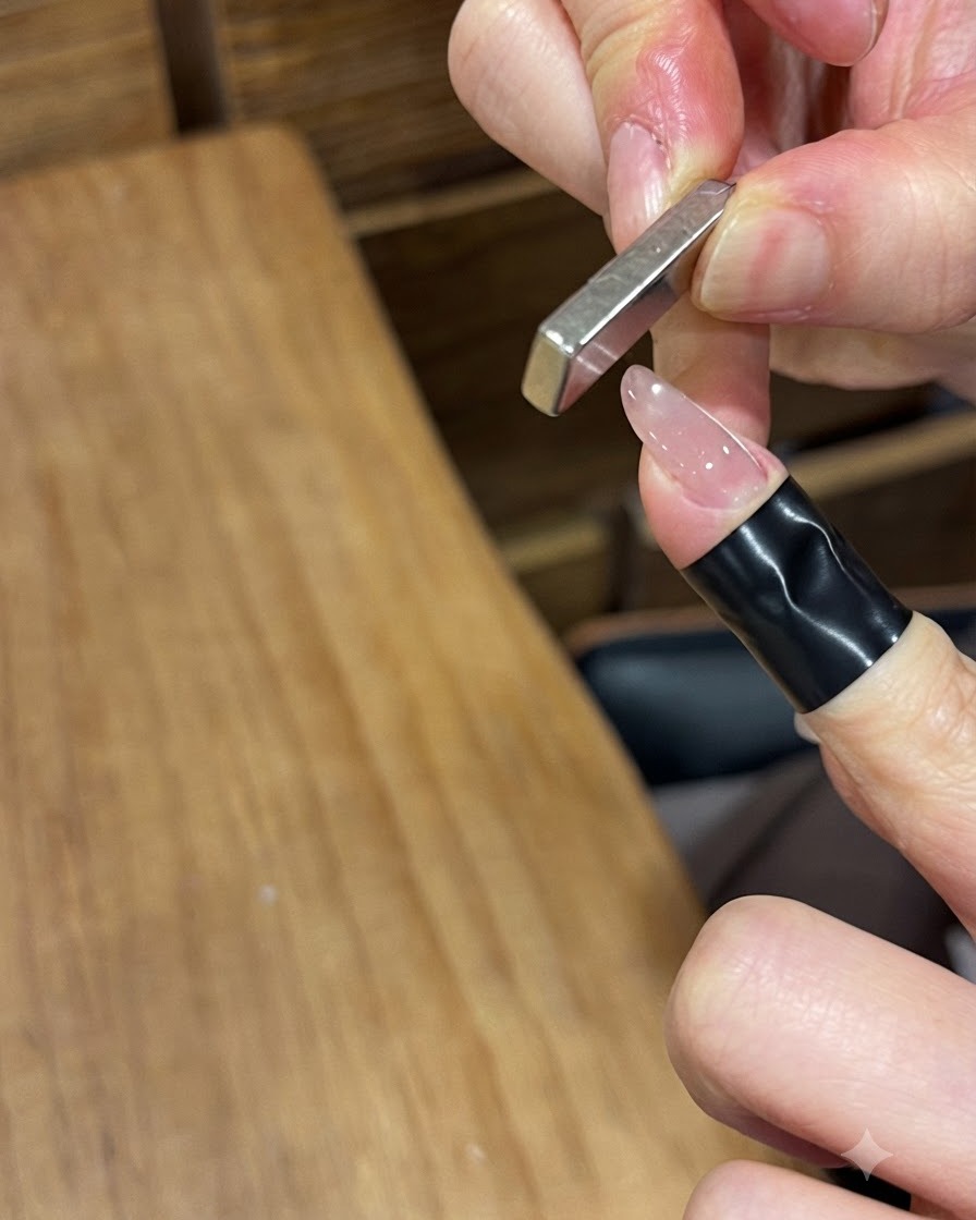 Un magnete a barra metallica rettangolare tenuto verticalmente vicino a ununghia dipinta in gel lucido per spingere le particelle magnetiche.