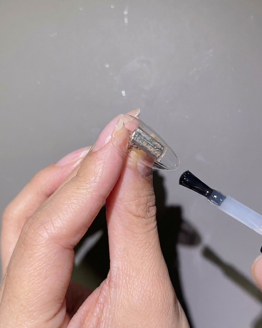 Un primo piano di un pennello per unghie che applica un gel rinforzante trasparente su una tip trasparente.