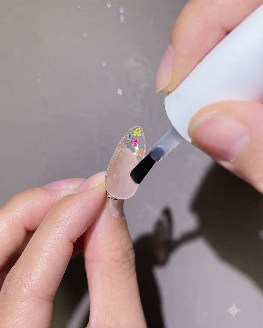 Un pennellino che applica una goccia precisa di top coat trasparente sulla nail art floreale di ununghia.