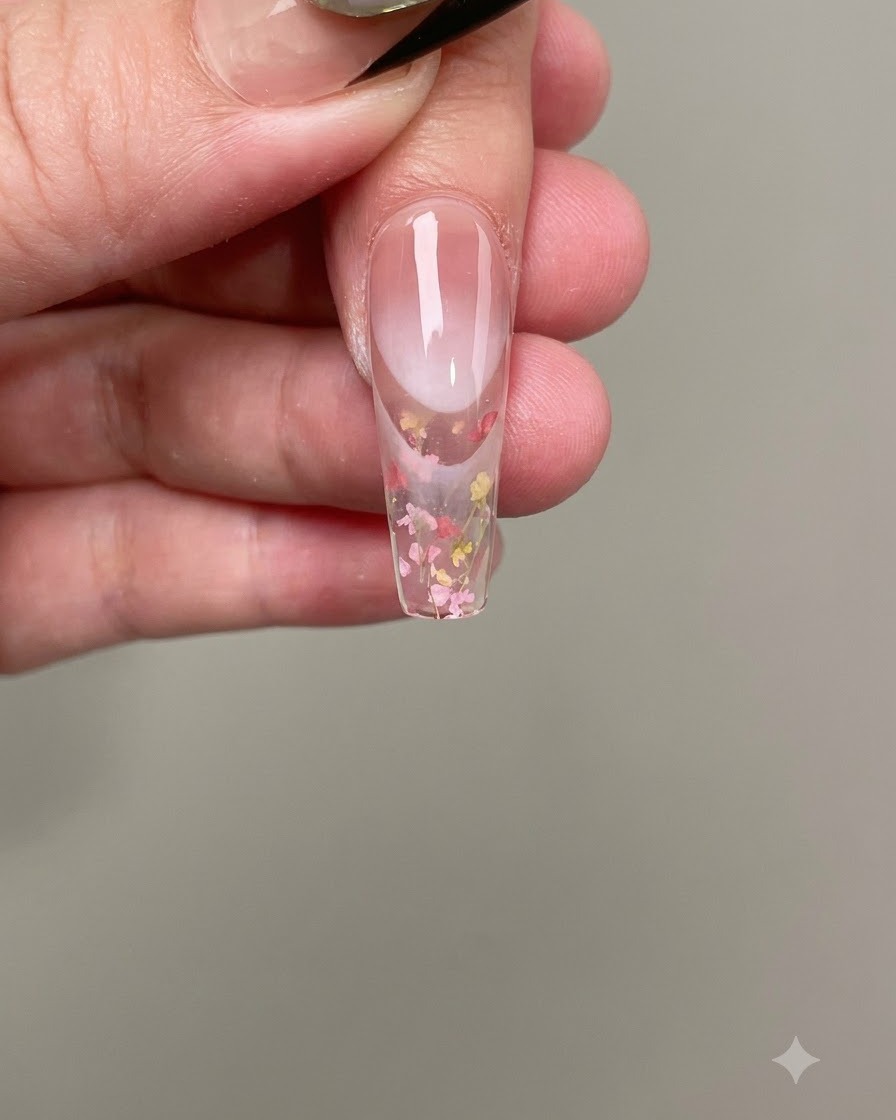 Una pinzetta posiziona piccoli fiori secchi rosa e gialli sul gel per unghie bagnato.