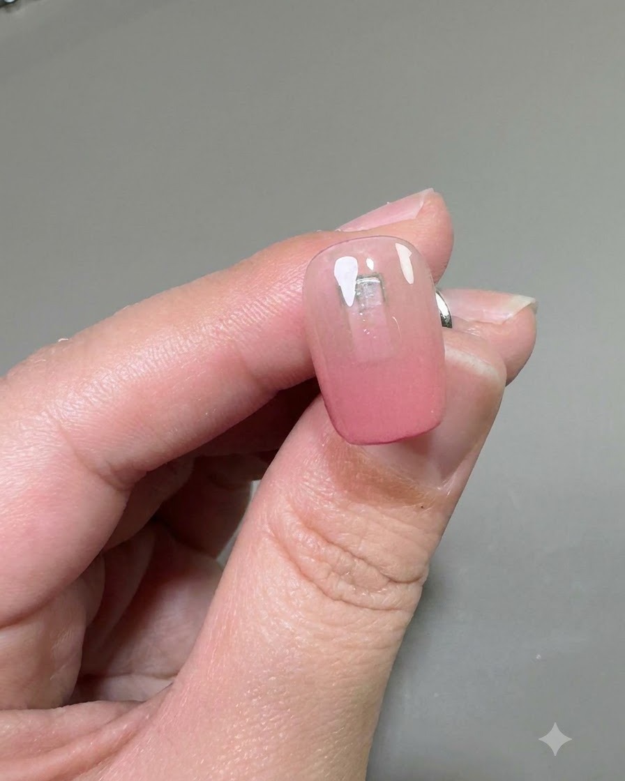 Un primo piano di ununghia che mostra una mano di gel rinforzante trasparente applicata sopra la base sfumata rosa.
