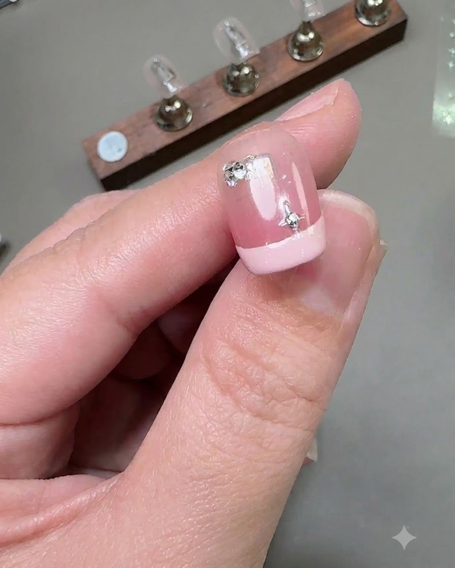 Una vista in primo piano di ununghia corta con French manicure caratterizzata da un adesivo a stella argentata e un piccolo diamante rotondo applicato vicino alla zona delle cuticole.