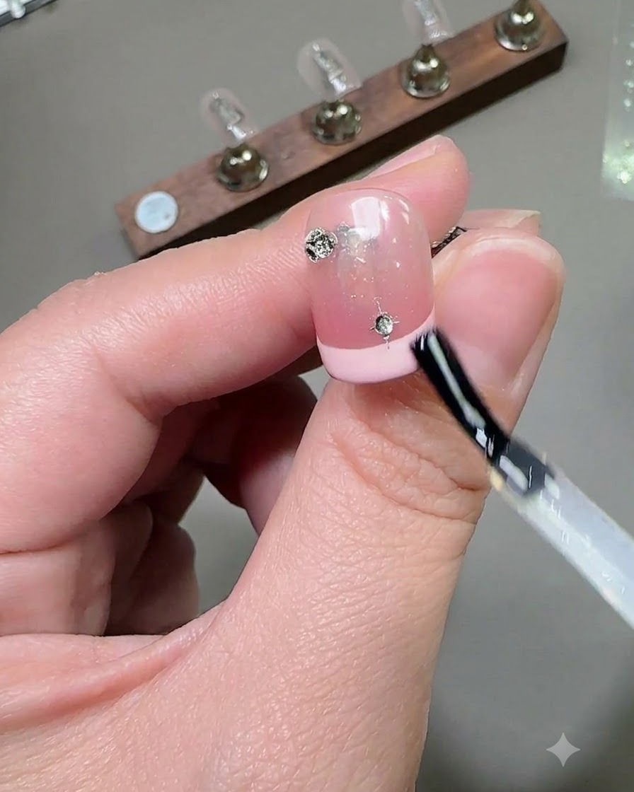 Un pennello che applica uno strato di top coat lucido sopra ununghia decorata con strass e ciondoli a stella.