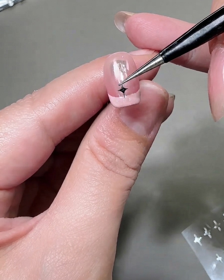 Uno strumento sottile che posiziona un adesivo a stella argentata sulla punta di una seconda unghia con French manicure.