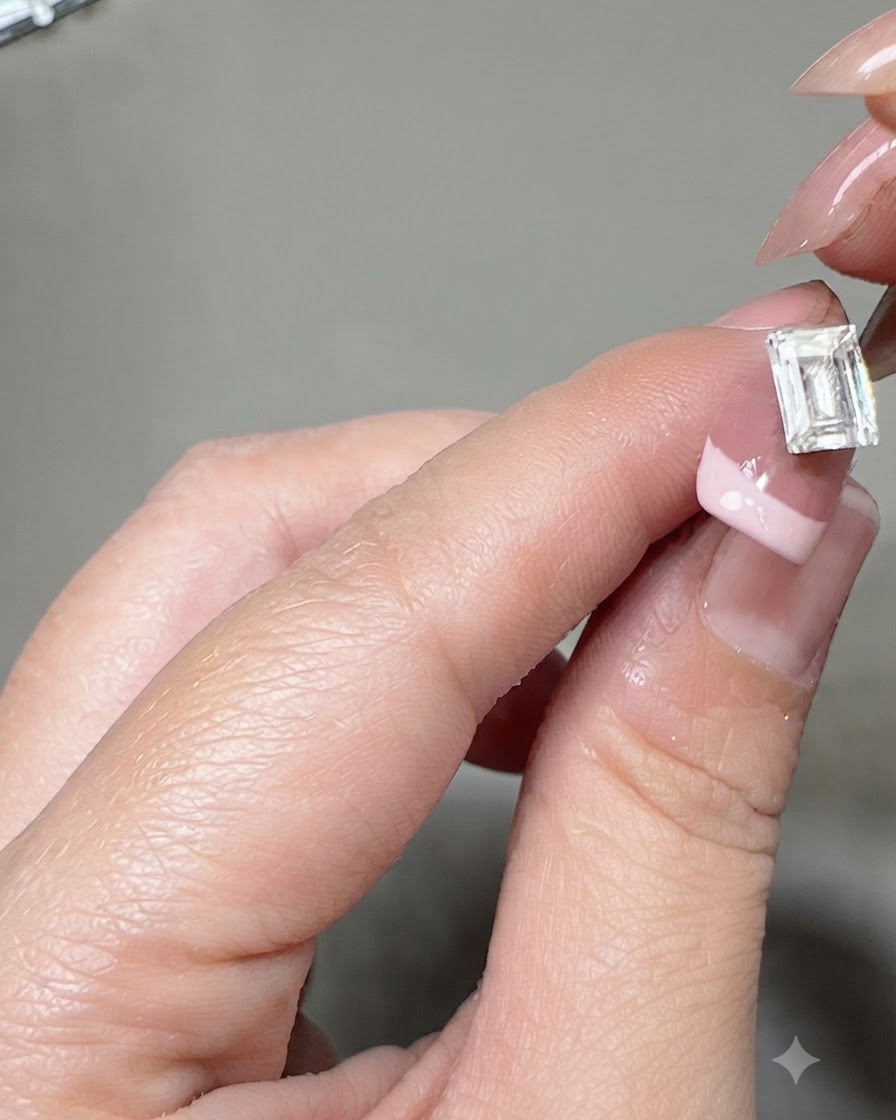 Un paio di pinzette che posizionano una grande gemma di cristallo rettangolare al centro di ununghia con French manicure.