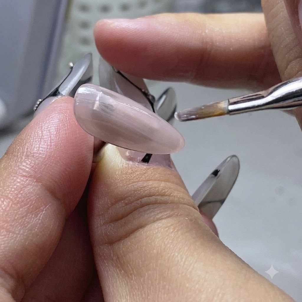 Un pennello piatto applica uno strato sottile di gel base color nude su un dito di unghia di pratica.
