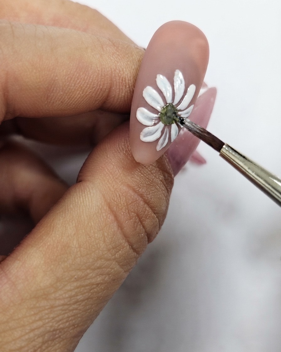 Primo piano di un pennello sottile che rifinisce il punto giallo centrale della nail art con margherita bianca.