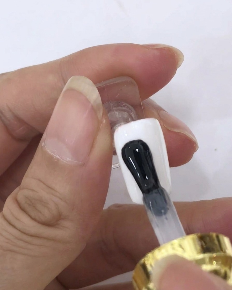 Un pennello applica uno strato trasparente di blooming gel sulla superficie di ununghia dipinta di bianco.