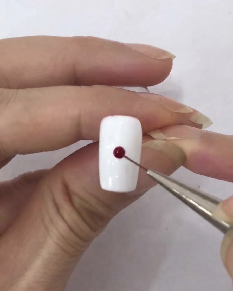 Un pennellino liner raccoglie una piccola goccia di smalto gel rosso scuro.