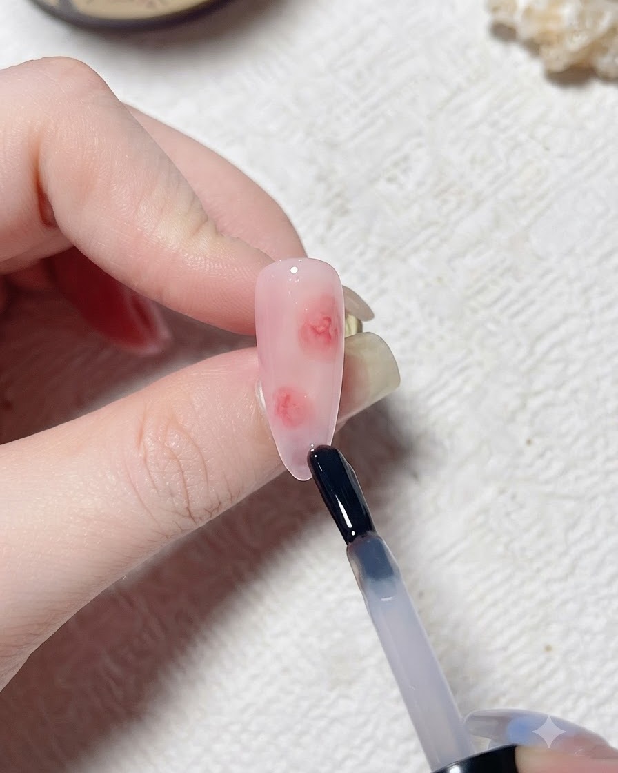 Un pennello applica uno strato trasparente di blooming gel su ununghia artificiale dai toni rosa.