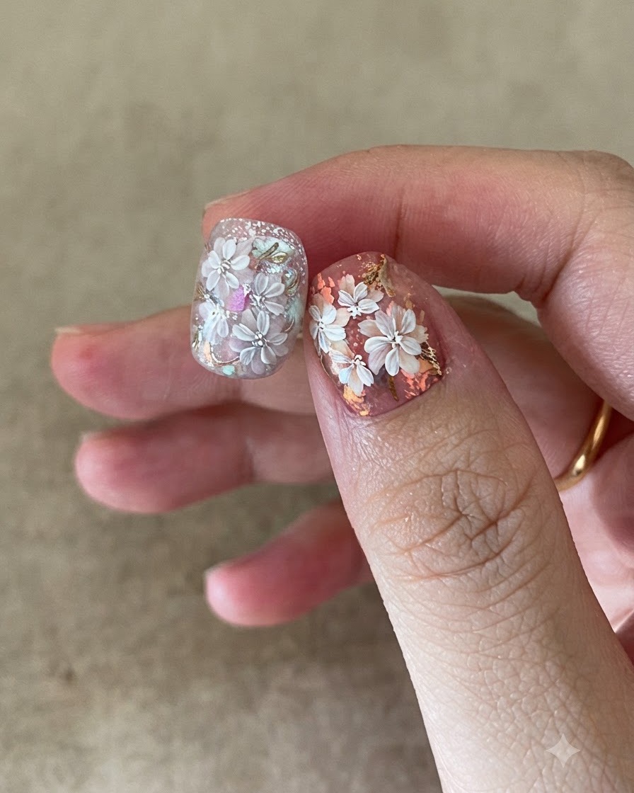 Un pennello per unghie applica un top coat trasparente su una complessa nail art floreale e in foglia oro.