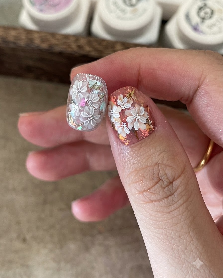 Un pennello fine per nail art aggiunge petali bianchi dettagliati su un design floreale preesistente.