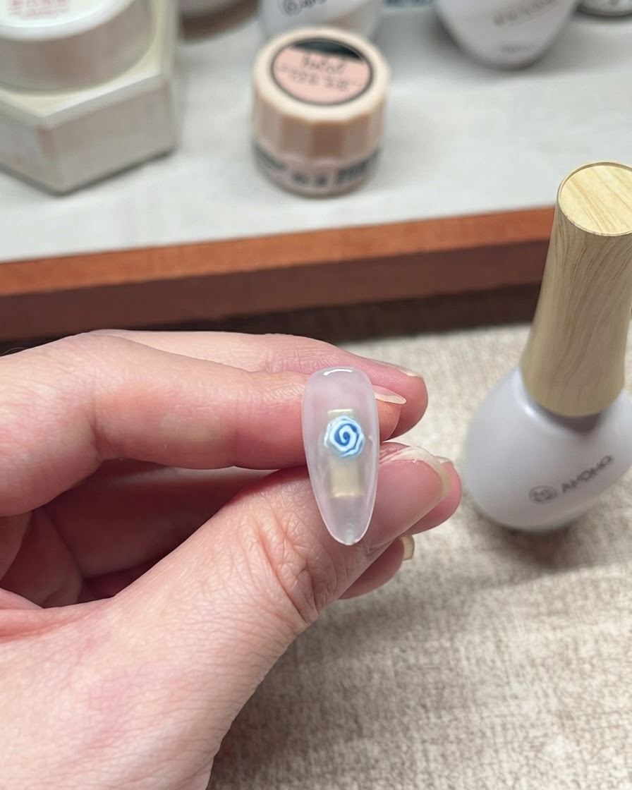 Primo piano di un design finito di unghie con rosa blu in gel accanto a un flacone bianco di prodotto per unghie.