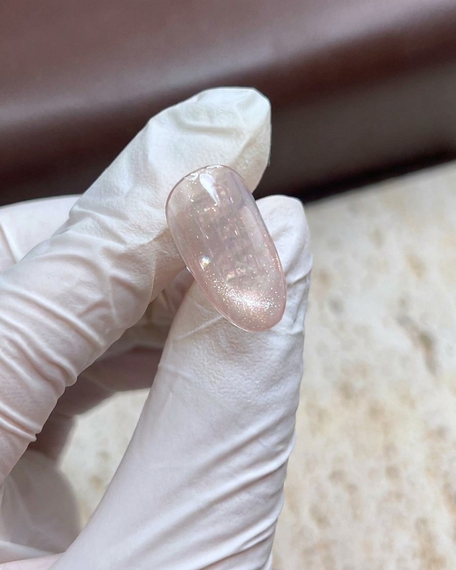 Una mano con i guanti che tiene un bastoncino magnetico sopra ununghia in gel cat-eye brillante per creare un effetto perla.