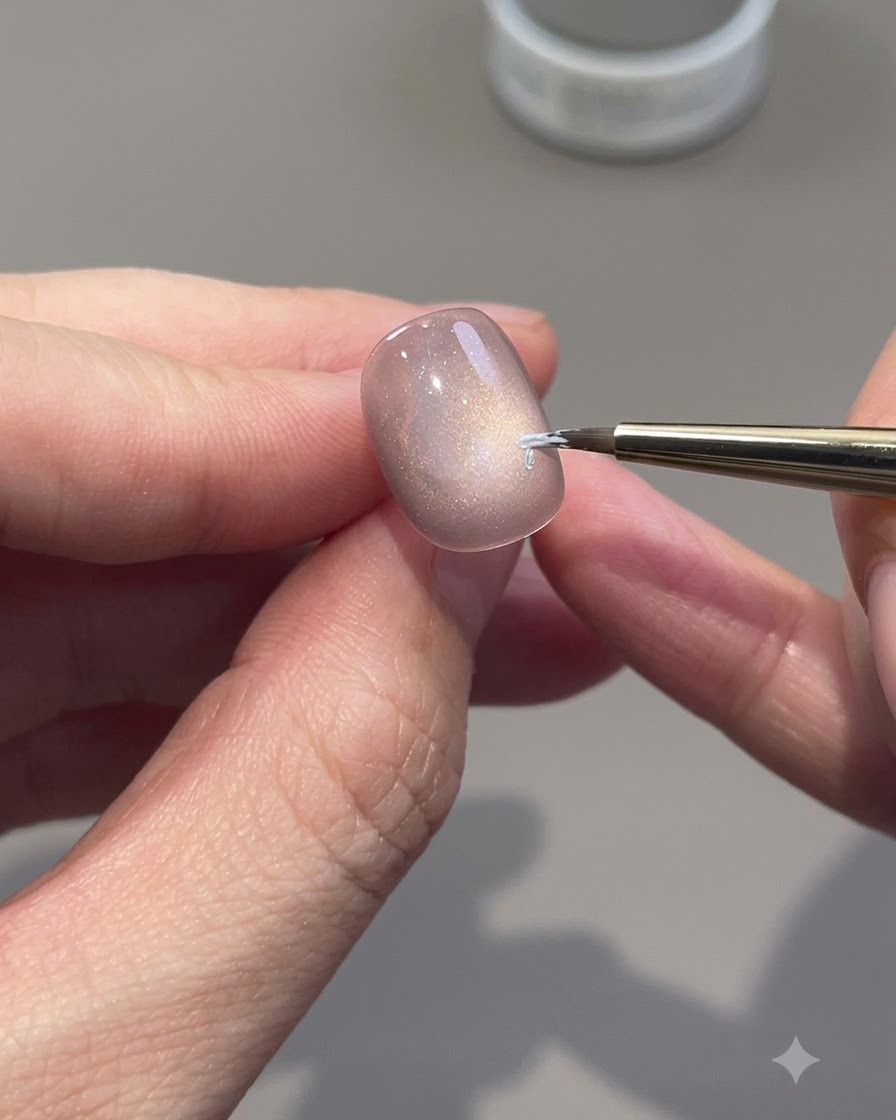 Un pennello a punta fine che disegna contorni di rose bianche su unghia in gel cat-eye.