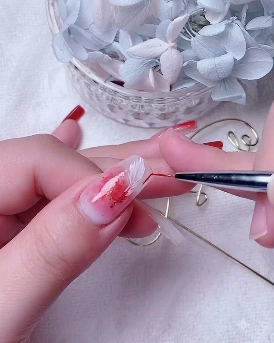 Primo piano di unonicotecnica che utilizza un pennello sottile per sfumare il gel rosso su ununghia con base bianco latte.