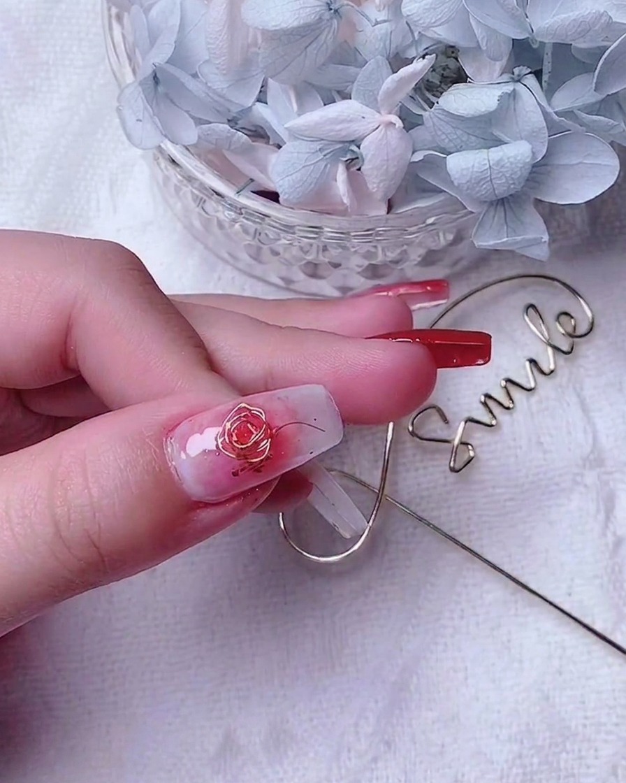 Primo piano di ununghia del pollice decorata con una rosa in filo doro e piccoli fili daccento lungo il bordo.