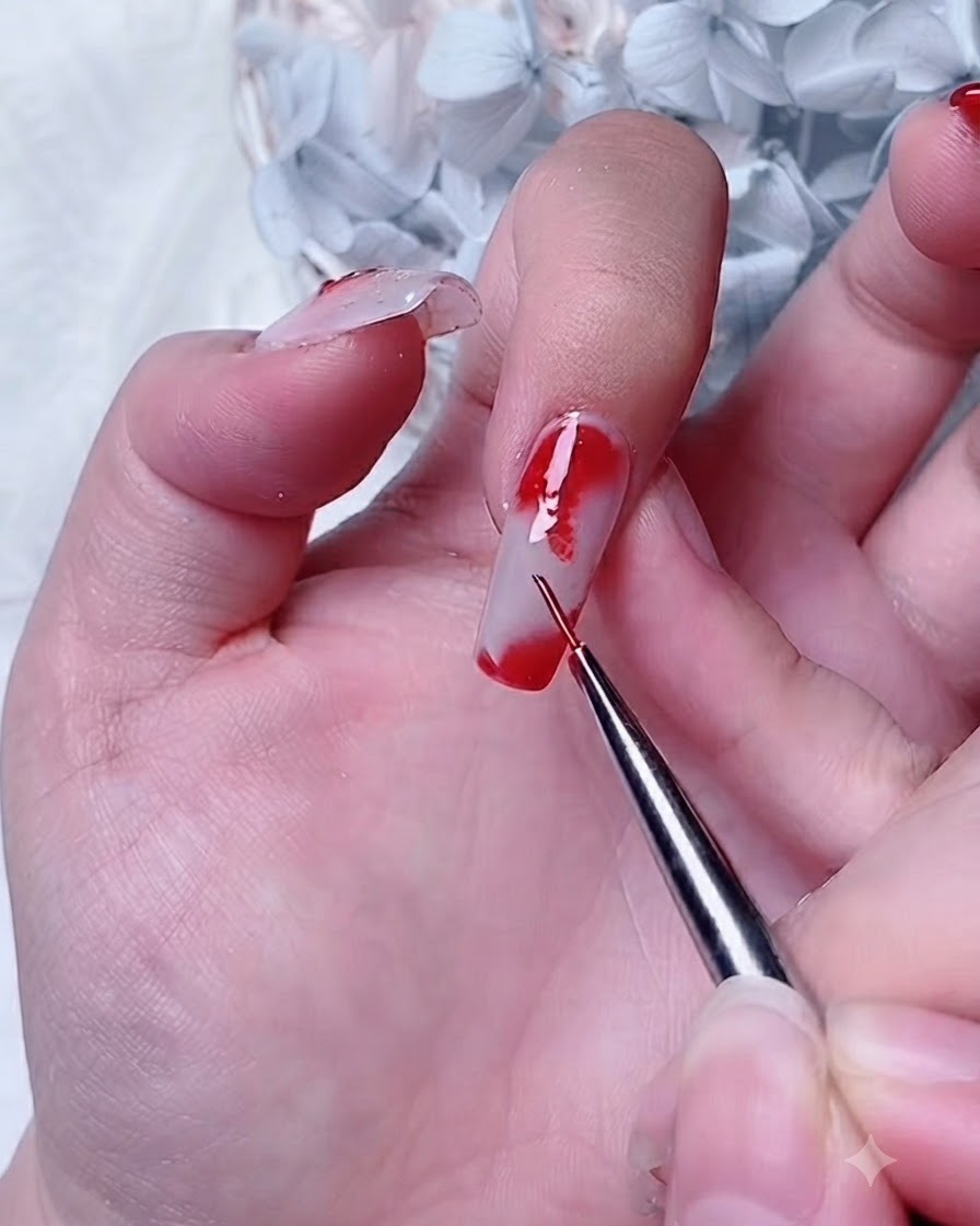 Un pennello da dettagli che applica il gel rosso su uno strato di blooming gel allangolo di ununghia dellindice.
