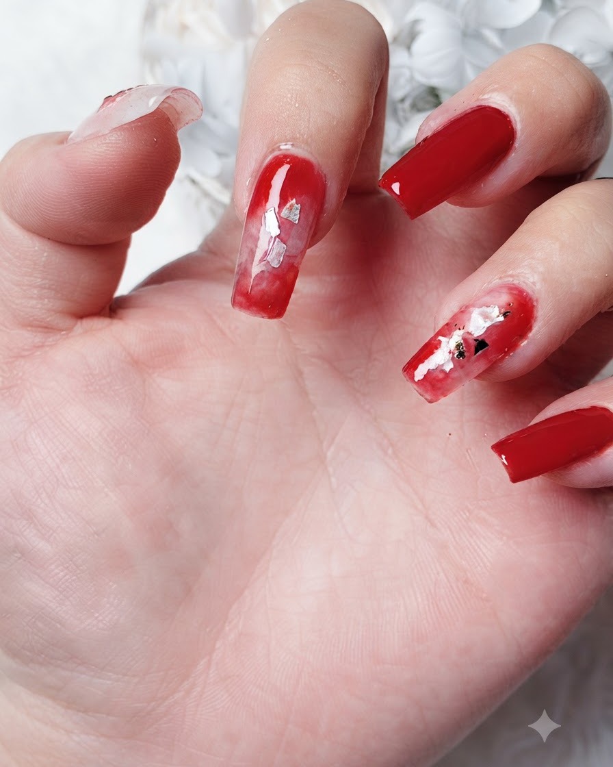 Primo piano di piccoli pezzi di lamina doro a forma di foglia posizionati in unarea di blooming gel rosso diffuso su ununghia.