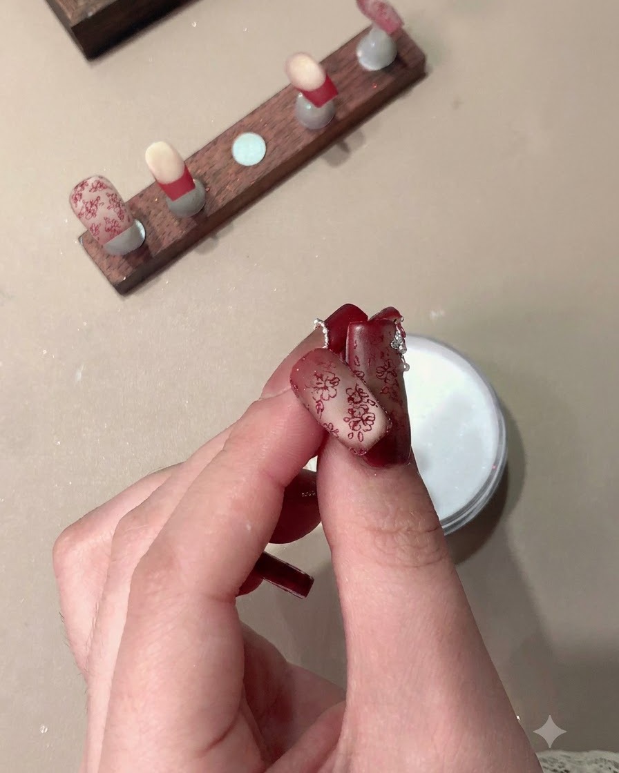 Una mano che mostra unghie press-on finite con motivi rossi stampati e french tip.